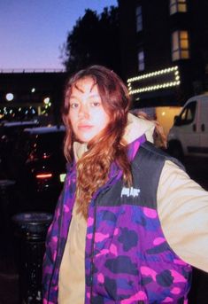 a woman in a purple and black jacket standing next to a parking lot at night