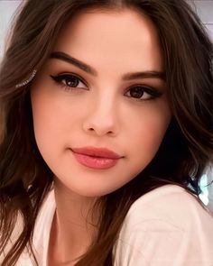 a woman with long hair wearing a white shirt and brown eyeshadow is looking at the camera