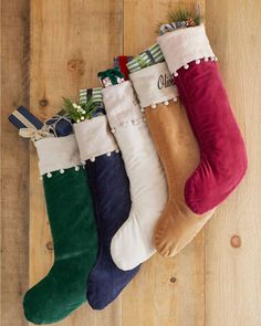 four christmas stockings with pom poms hanging from them on a wooden floor,