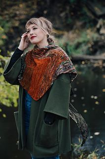 a woman standing next to a river talking on a cell phone and wearing a shawl