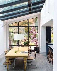 a dining room table with chairs and a lamp in front of large windows that look out onto the backyard