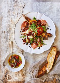 a white plate topped with meat and veggies next to bread