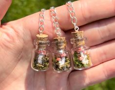 three tiny glass bottles filled with different types of plants and rocks are held in the palm of a person's hand