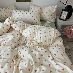 a bed with pink hearts on it in a bedroom next to a nightstand and pictures