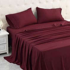 a bed covered in maroon sheets and pillows