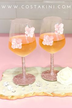 two wine glasses sitting on top of a pink tray with white flowers in the middle