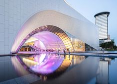 a large building with a purple light on it's side next to a body of water