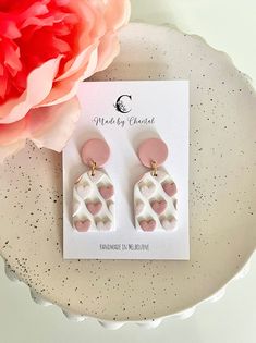 a pair of pink and white heart shaped earrings sitting on top of a plate next to a flower