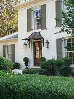 a white brick house with green shutters and potted plants on the front porch