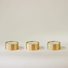 three gold candles sitting next to each other on a white surface with one candle in the middle