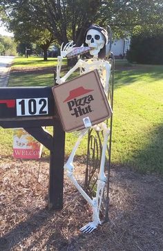 a skeleton holding a pizza hut sign in front of a mailbox on the side of a road