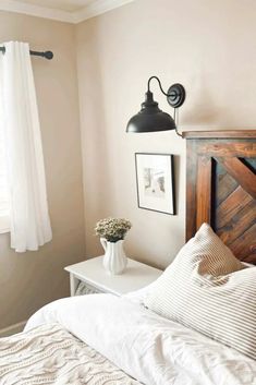 a bed with white sheets and pillows in a bedroom next to a lamp on the wall