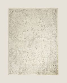 an antique rug with white and grey colors on the ground, in front of a beige background