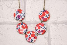 three red and blue flowers are hanging from a gold chain on a white brick wall