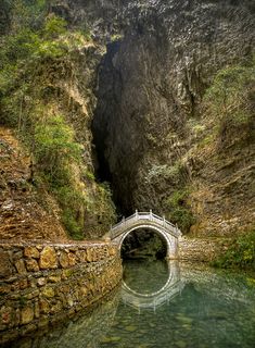 a bridge that is over some water in the middle of a mountain area with green trees