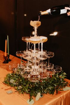 champagne being poured into wine glasses on top of a table with greenery and candles