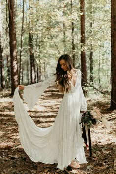 a woman in a white dress is walking through the woods with her long sleeves open