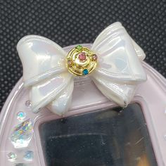 Elevate your Tamagotchi P's look to magical heights with our custom Deco Pierce, adorned with the iconic Sailor Moon bow. These bows are a brand new style featuring a beautiful iridescent gloss effect and come in a variety of colors to match your Tama perfectly! There are now several different new brooch charms to choose from! We now have  Luxe Crystal Star Compacts (white or multi-colored stones), Season 1 compacts (Sailor Moon Crystal), Crystal Star Compacts, Crisis Moon Compacts, Cosmic Heart Compacts, Star Charms, and Cardcaptor Sakura charms Available in a spectrum of pastel iridescent shades - purple, blue, green, yellow, dark pink, light pink, and white - this Deco Pierce isn't just a stylish statement, it's a magical gateway to a world where nurturing and nostalgia collide. You can Sailor Moon Bow, Cosmic Heart, Sailor Moons, Moon Princess, Virtual Pet, Pet Style, Moon Crystal, Colored Stones, Sailor Moon Crystal