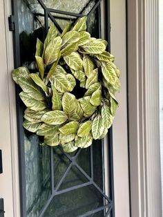 a wreath hanging on the front door of a house with green leaves and metal frame