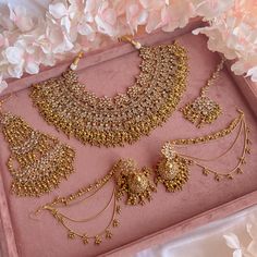 a pink tray with some gold jewelry on it and white flowers in the back ground