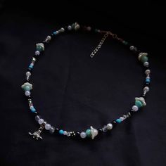 Beaded necklace with a dinosaur charm. Color palette: white, black, gree. blue. Length: 43cm +5cm chain extention. The necklace ends with a lobster claw closure. turquoise stone beads. the necklace is beaded on a stainless steel thread.