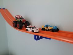 two toy trucks are on top of a shelf with an orange track and blue car