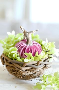 a small bird figurine sitting on top of a basket filled with green leaves