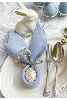 a white plate topped with a blue napkin and bunny figurine next to silverware