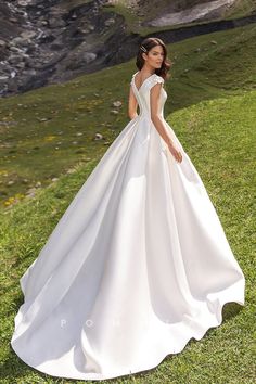 a woman in a white wedding dress standing on the side of a hill with her back to the camera