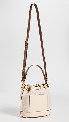 Find TORY BURCH T Monogram Bucket Bag on Editorialist. This Tory Burch bucket bag features a structured silhouette with gold-tone hardware. The bag is crafted from jacquard with a monogram pattern and leather trim. It has a drawstring top, patch interior pocket, and an optional adjustable strap. The bag is lined in suede and has a height of 8.25 inches, a length of 8.25 inches, and a depth of 4.75 inches. The strap drop is 21.75 inches and the handle drop is 4 inches. Elegant Bucket Bag With Brass Hardware, Beige Monogram Canvas Bag With Gold-tone Hardware, Luxury Bucket Bag With Brass Hardware, Elegant Top Handle Bucket Bag With Brass Hardware, Gold Monogram Canvas Crossbody Shoulder Bag, Designer Cream Bucket Bag With Detachable Handle, Gold Monogram Canvas Shoulder Bag With Double Handle, Gold Monogram Canvas Shoulder Bag With Dust Bag, Luxury Double Handle Bucket Bag With Gold-tone Hardware