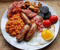 a white plate topped with eggs, sausages and beans next to tomatoes on a table