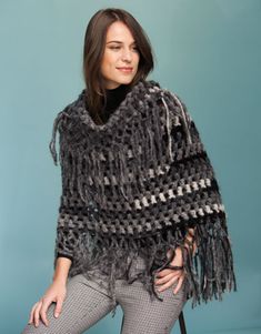 a woman sitting on a chair wearing a black and grey ponchy with fringes