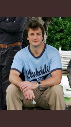 a man sitting on a bench next to a tree and another man standing behind him