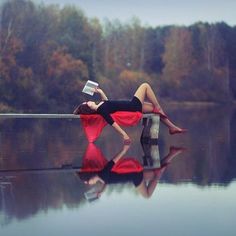 a woman is laying on the edge of a body of water while reading a book