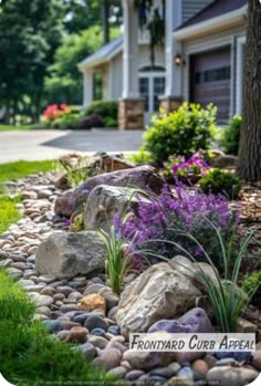 a rock garden with purple flowers in the foreground and a house in the background