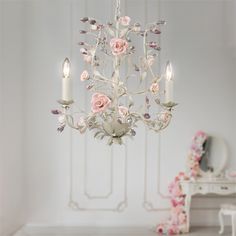 a white chandelier with pink roses hanging from it's center and two candles in the middle