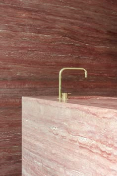 a bathroom sink with a gold faucet on top of it next to a red marble wall