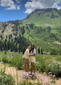 two girls standing in the middle of a field with mountains in the backgroud