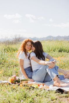 two women are sitting on a blanket in the middle of a field with orange flowers