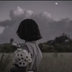 a woman standing in a field holding a bouquet of flowers and looking at the sky