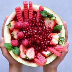 a person holding a fruit bowl filled with watermelon, strawberries and raspberries