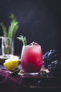 a red drink in a glass next to grapes and lemons