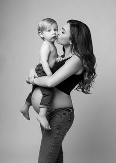 a woman is holding a baby and kissing her cheek in black and white, against a gray background