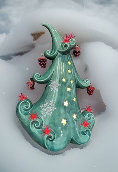 a ceramic christmas tree with pine cones on it's top in the middle of snow