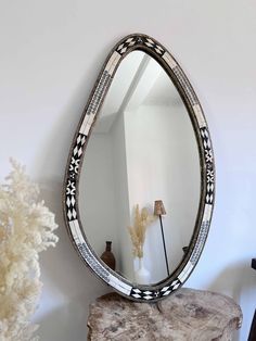 a mirror sitting on top of a wooden table next to a white vase and lamp