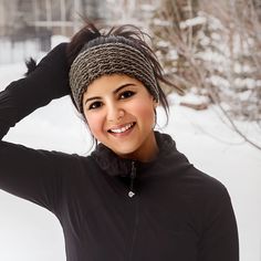 a smiling woman with her hair in a knitted headband and black jacket, standing outside in the snow