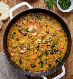 a pot filled with soup sitting on top of a wooden table next to some bread