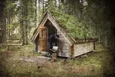 a man standing in the doorway of a small wooden cabin with moss growing on it's roof