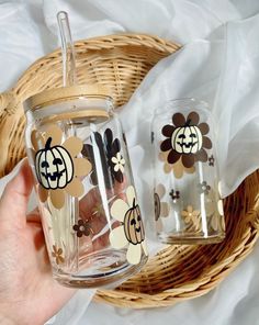 two glass jars with pumpkins on them sitting next to each other in front of a wicker basket