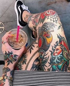 a person with tattoos holding a drink in their hand